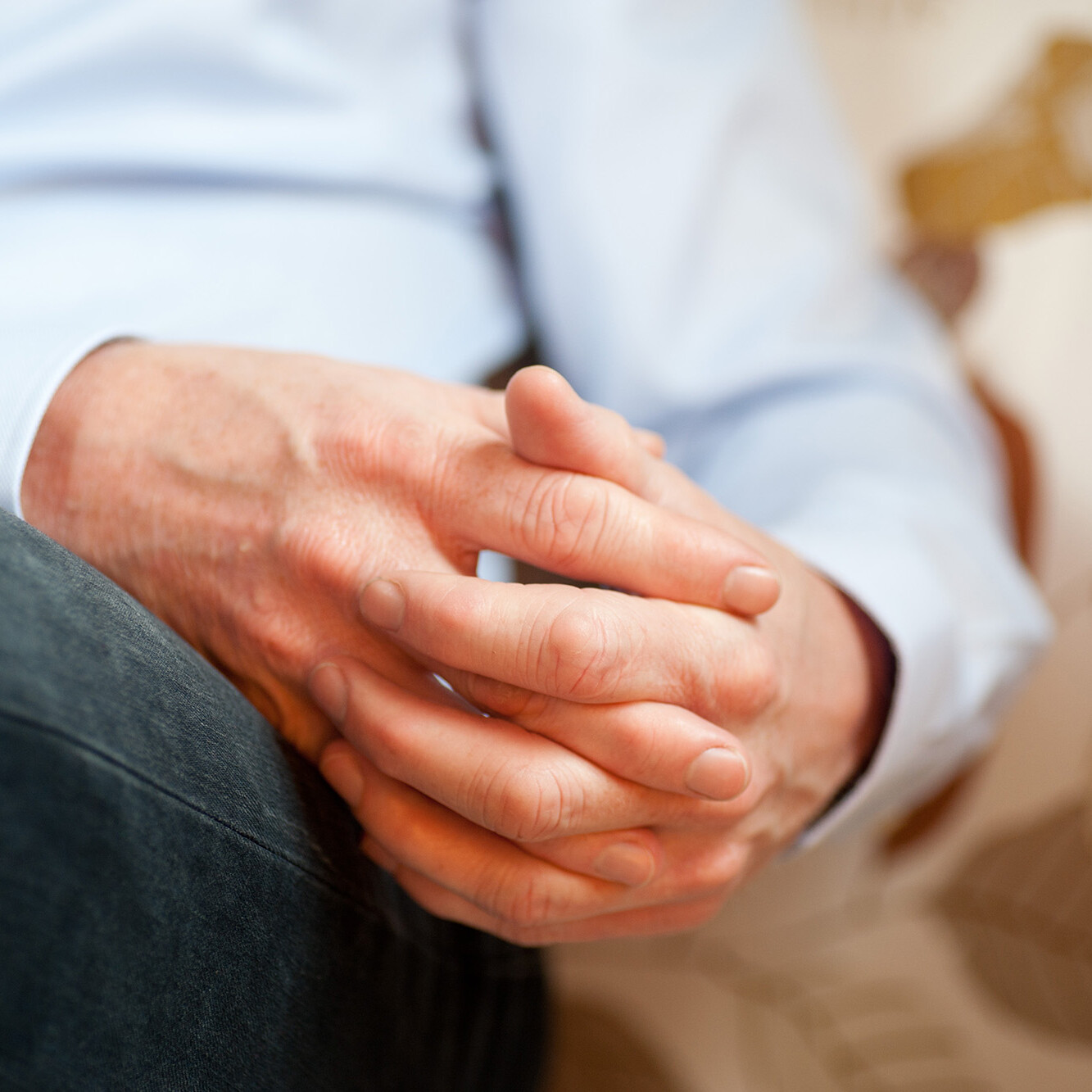 Verschränkte Hände eines Therapeuten auf hellem Sofa – Symbol für Aufmerksamkeit, Ruhe und Vertraulichkeit im Therapieraum