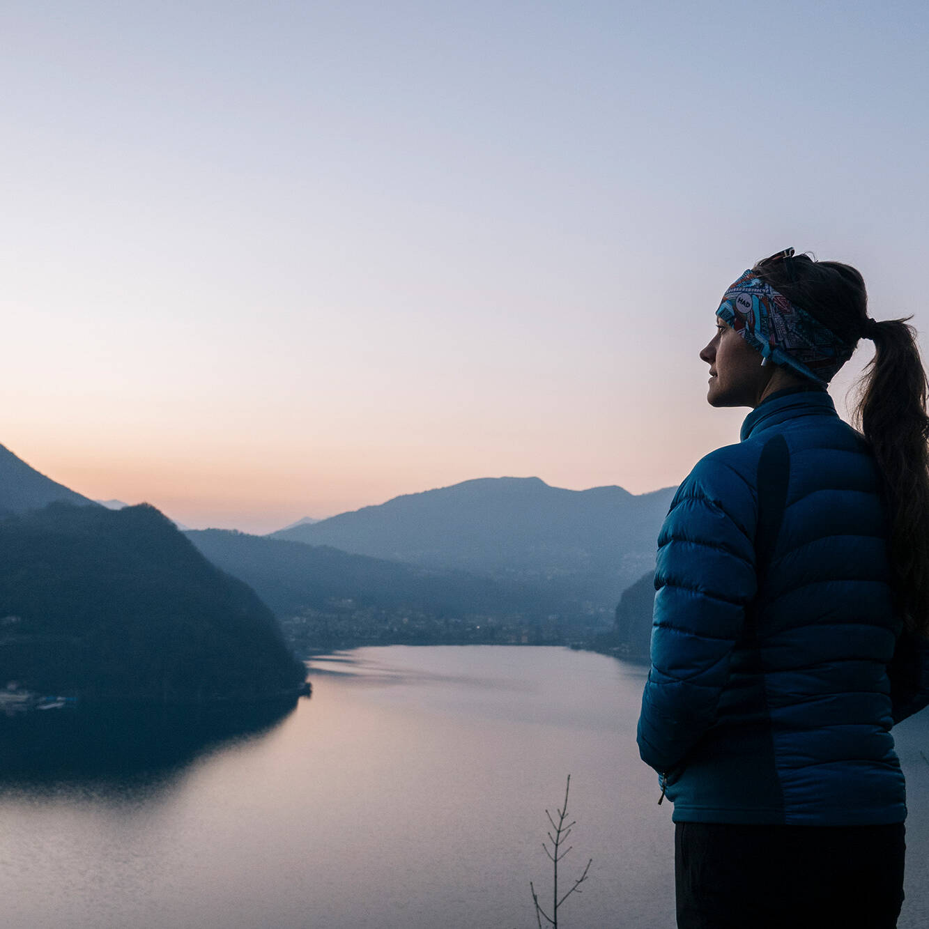 Frau blickt in Wanderkleidung über einen ruhigen See bei Sonnenuntergang – Berge im Hintergrund