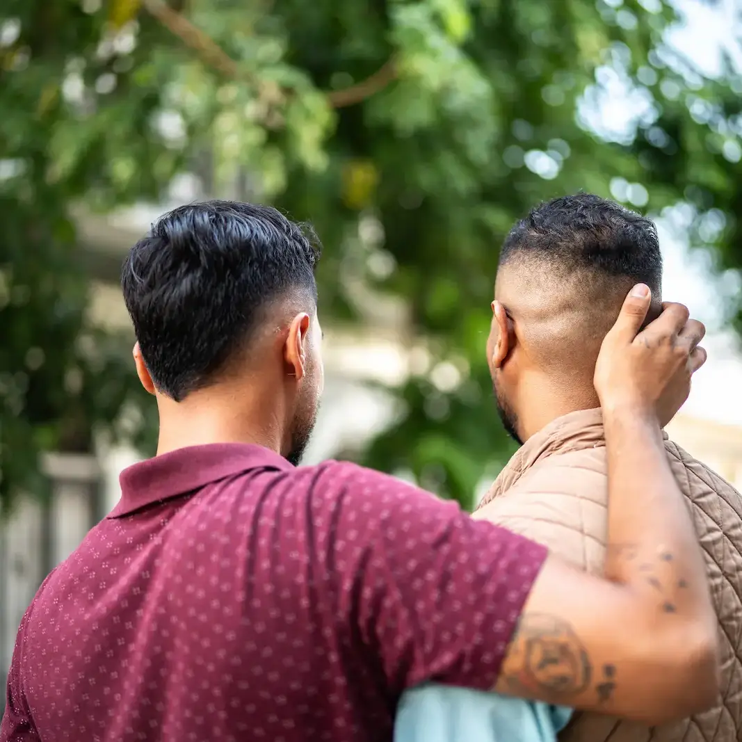 Zwei Menschen gehen nebeneinander, einer legt dem anderen beruhigend die Hand auf den Nacken