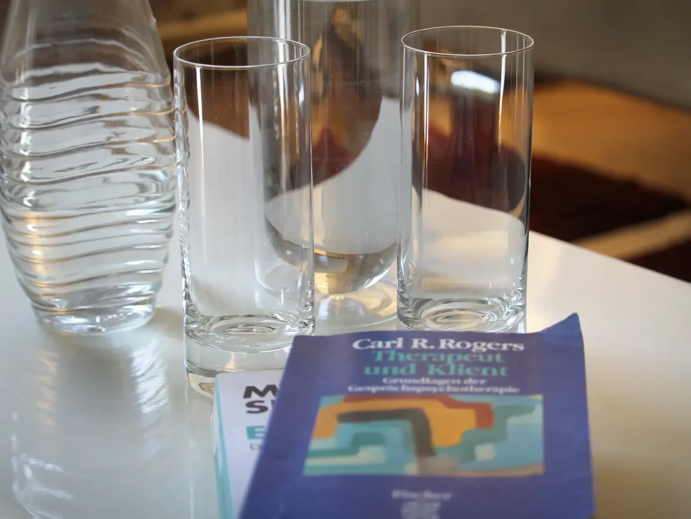Buch von Carl R. Rogers neben Wassergläsern auf dem Tisch der Praxis Niederreiter